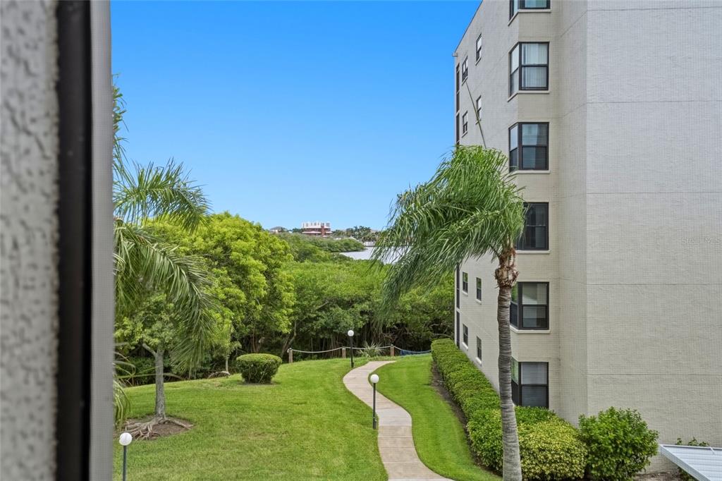 A view from a balcony overlooking a grassy lawn, a winding path, and distant water — 1328 PASADENA AVENUE S UNIT 308, SOUTH PASADENA, FL