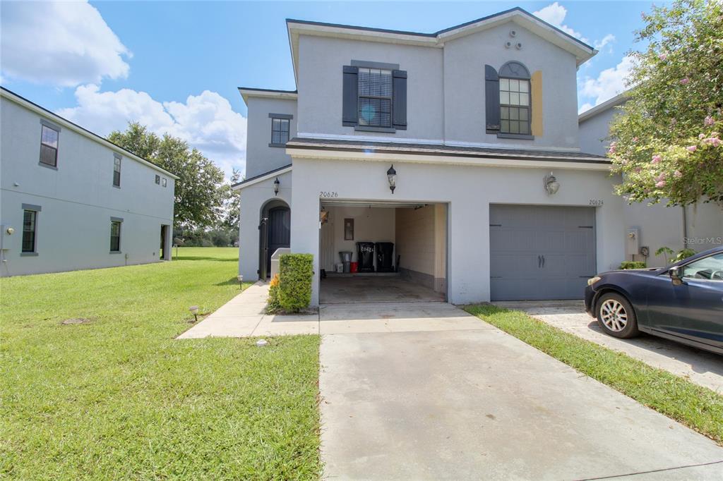 A two-story gray house features an open garage, a driveway, and a side lawn — 20626 MAXIM PARKWAY, ORLANDO, FL