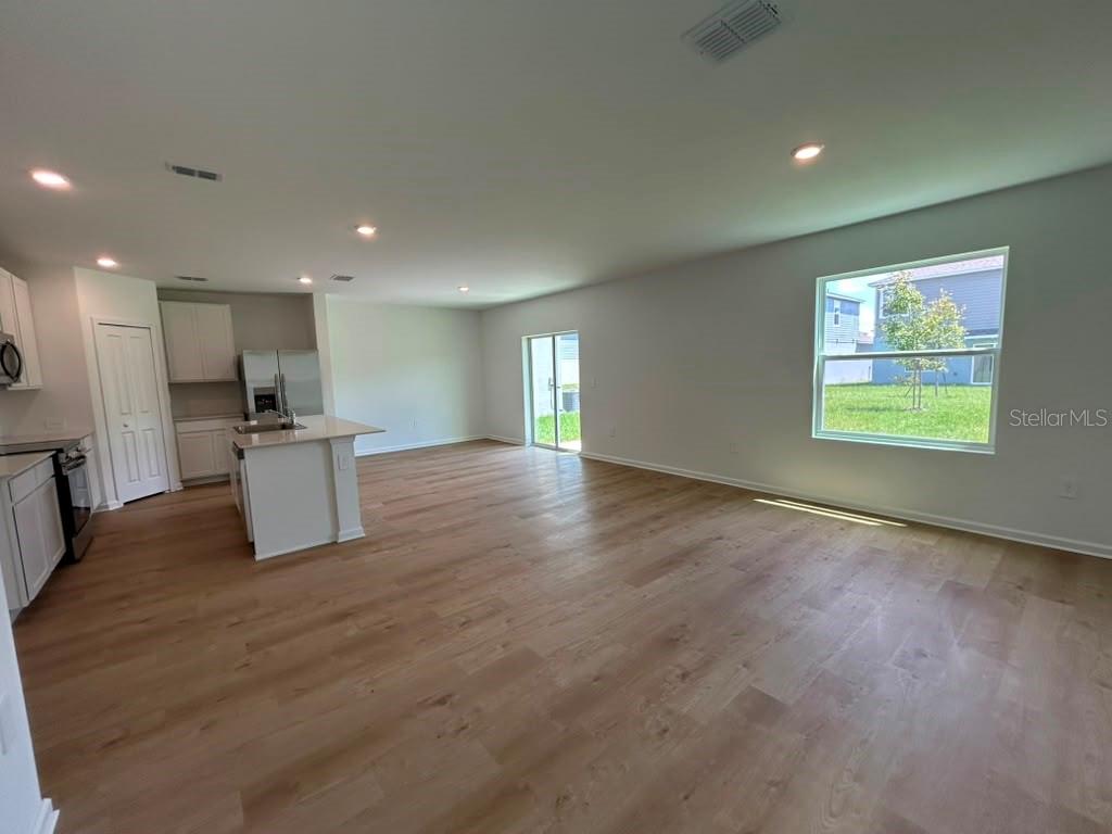 An open-concept kitchen and living area features light wood flooring, white cabinetry, and sliding doors — 6268 BOTTICELLA BOULEVARD, WINTER HAVEN, FL