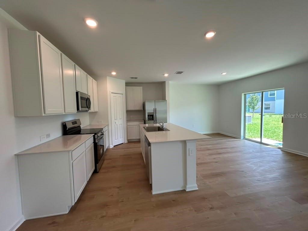 A modern kitchen features white cabinets, stainless steel appliances, a center island, and wood flooring — 6268 BOTTICELLA BOULEVARD, WINTER HAVEN, FL
