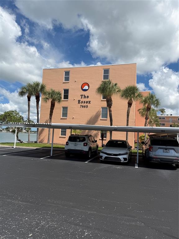 A multi-story peach-colored apartment building stands behind a covered parking area with three cars — 7665 SUN ISLAND DRIVE S UNIT 409, SOUTH PASADENA, FL