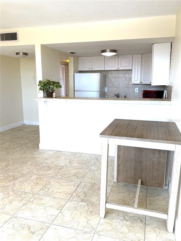 A kitchen with white cabinets and a tile floor features a breakfast bar and table — 7665 SUN ISLAND DRIVE S UNIT 409, SOUTH PASADENA, FL