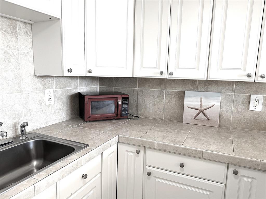 A kitchen features white cabinets, a tiled countertop and backsplash, and a stainless steel sink — 7665 SUN ISLAND DRIVE S UNIT 409, SOUTH PASADENA, FL