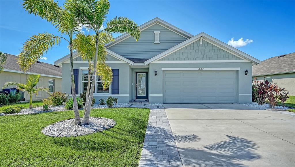 A light blue single-story house features a two-car garage, a palm tree, and landscaped beds — 10402 CHARLOTTE DRIVE, PARRISH, FL
