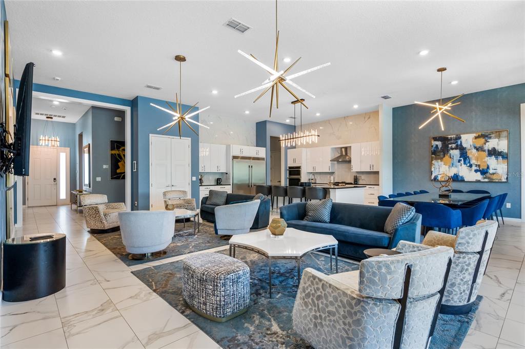 A spacious open-concept living and dining area features blue accents, modern chandeliers, and marble flooring — 1758 OAK BLOSSOM DRIVE, DAVENPORT, FL