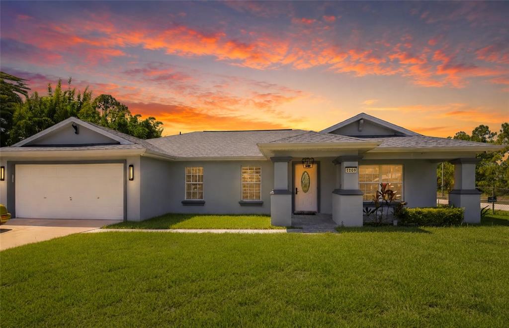 A single-story house with a white garage, gray siding, and a front porch at sunset — 1104 MORTON STREET E, LEHIGH ACRES, FL