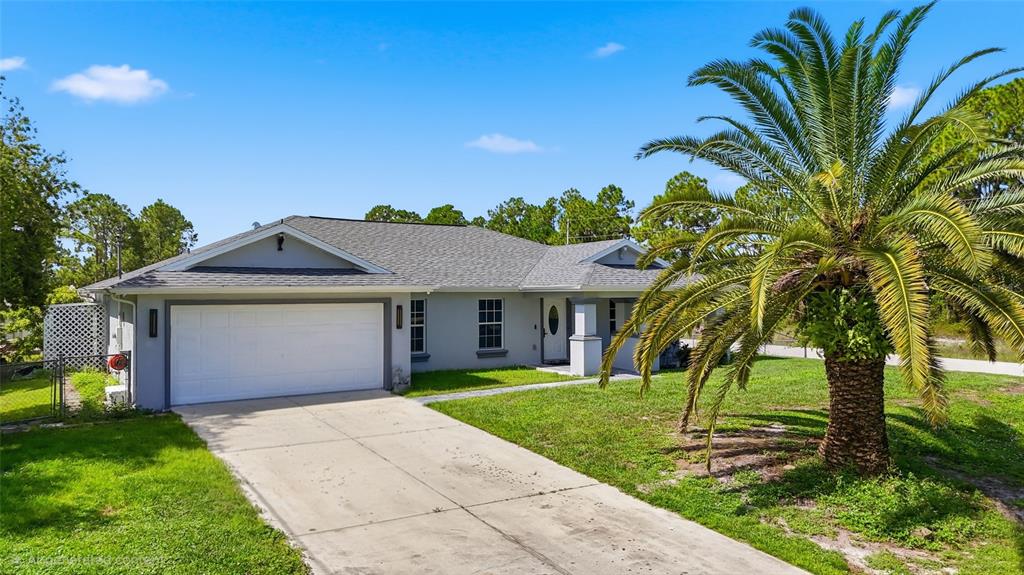 A single-story house with a white garage door and a large palm tree in front — 1104 MORTON STREET E, LEHIGH ACRES, FL