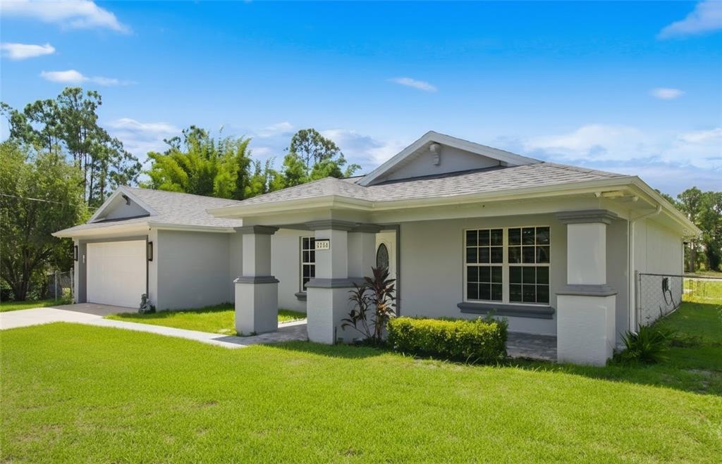 A single-story house with a gray exterior, a front porch, and an attached two-car garage — 1104 MORTON STREET E, LEHIGH ACRES, FL