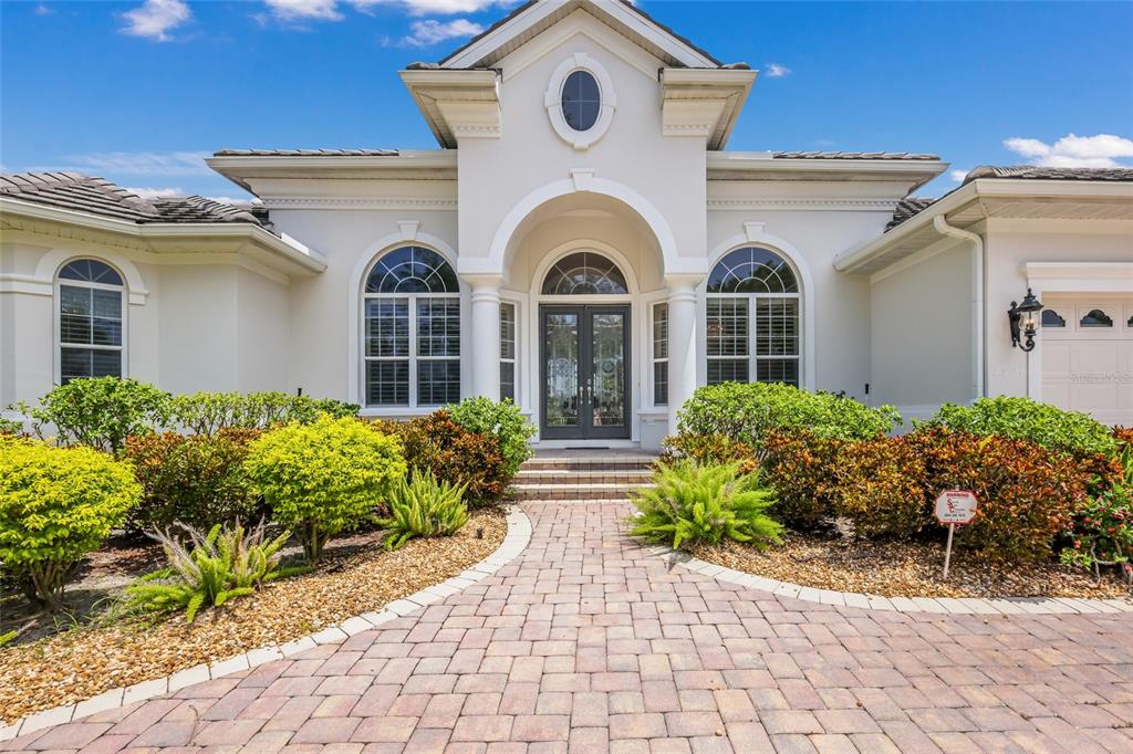 The exterior of a light-colored house features a brick walkway leading to a double-door entrance — 5904 RIVERVIEW BOULEVARD, BRADENTON, FL