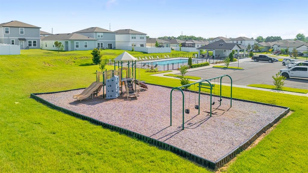 A playground with slides and swings sits on a wood-chipped lot near a community pool — 38465 HONEYSUCKLE DRIVE, DADE CITY, FL