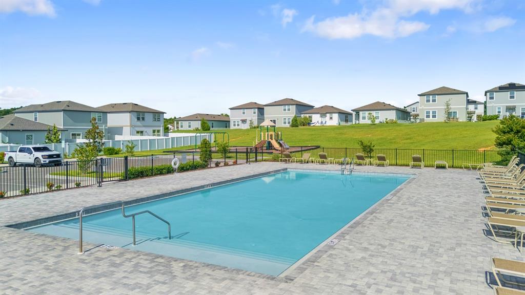 A community swimming pool with lounge chairs and a playground in the background — 38465 HONEYSUCKLE DRIVE, DADE CITY, FL