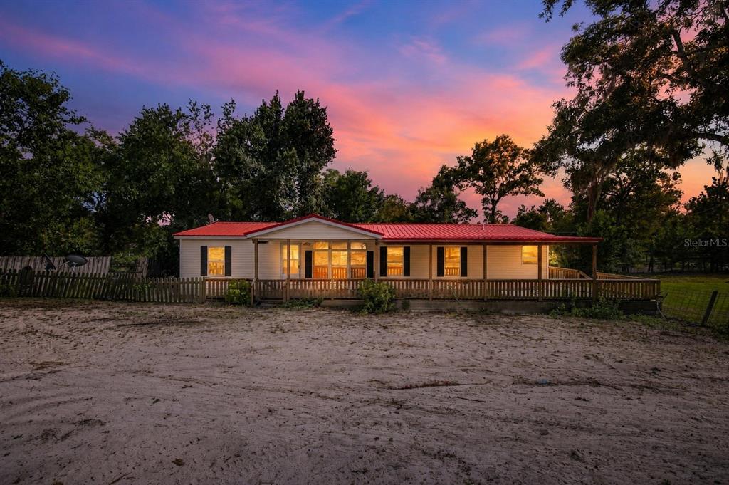 A single-story house with a red metal roof and a wooden porch at sunset — 2251 SE 136TH AVENUE, MORRISTON, FL