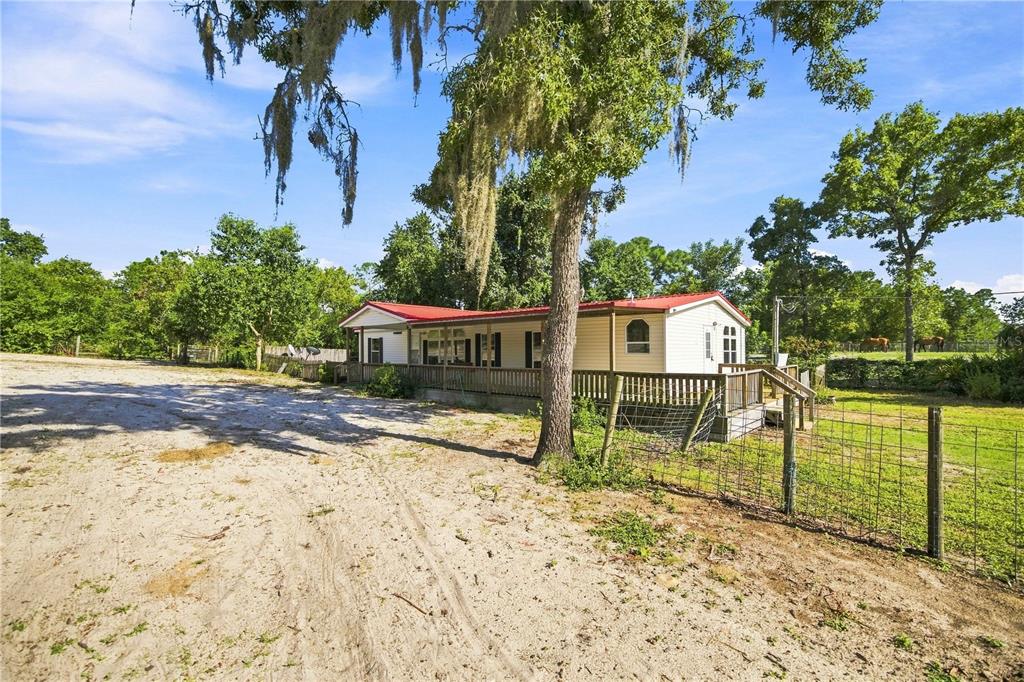 A single-story manufactured home with a red metal roof sits on a sandy, fenced lot — 2251 SE 136TH AVENUE, MORRISTON, FL