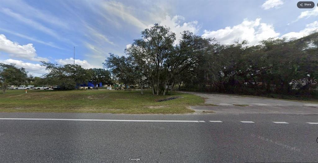 A vacant, grassy lot with mature trees and a paved driveway entrance from the road — N/A, POLK CITY, FL