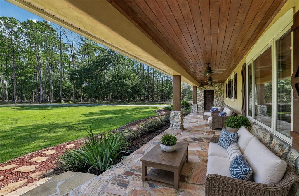 A covered stone patio features wicker furniture, a wood ceiling, and views of a grassy yard — 11450 FANGORN ROAD, ORLANDO, FL