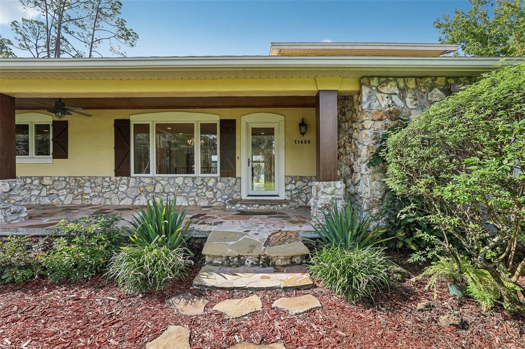 A stone-clad house exterior features a covered porch, a front door, and landscaped garden beds — 11450 FANGORN ROAD, ORLANDO, FL