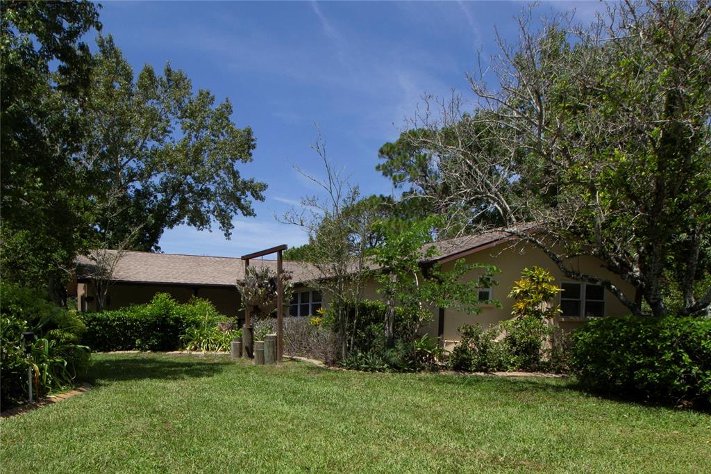 A tan single-story house with a shingled roof sits behind a grassy lawn and trees — 8609 HORIZON LANE, HUDSON, FL