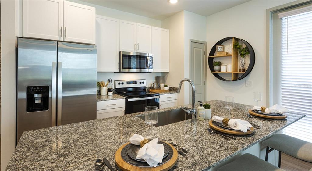 A kitchen features white cabinets, stainless steel appliances, granite countertops, and a central island — 4980 RED MAPLE LANE UNIT B1, WILDWOOD, FL
