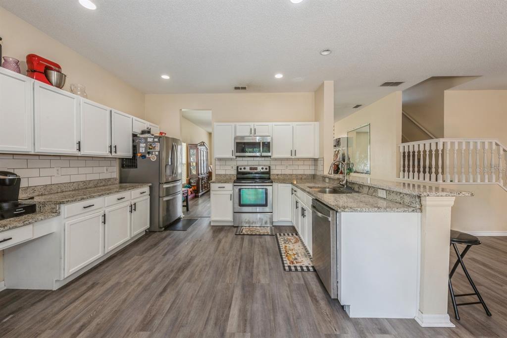 A kitchen with white cabinets, granite countertops, stainless steel appliances, and wood-look flooring — 502 FREEMAN STREET, LONGWOOD, FL