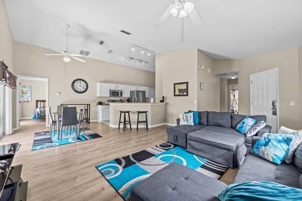 An open-concept living room and kitchen feature light wood flooring, a gray sectional, and blue accents — 641 RESERVE DRIVE, DAVENPORT, FL