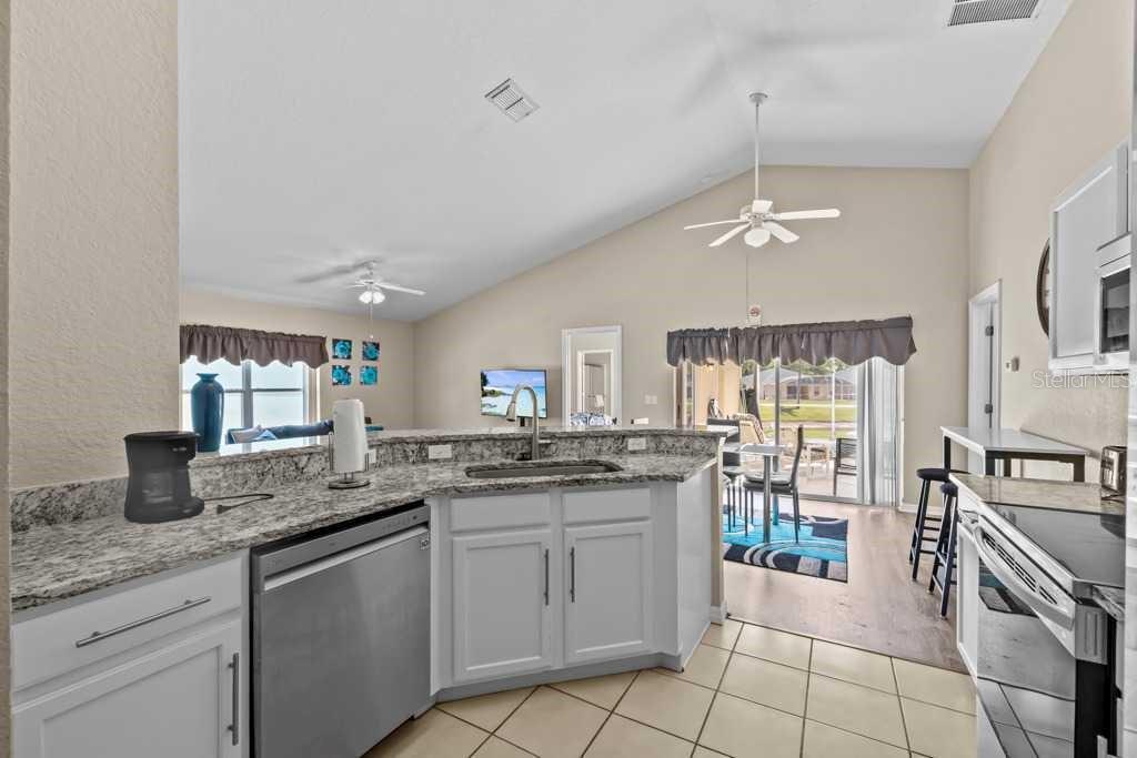 A kitchen with white cabinets, granite countertops, and a stainless steel dishwasher overlooks a living area — 641 RESERVE DRIVE, DAVENPORT, FL