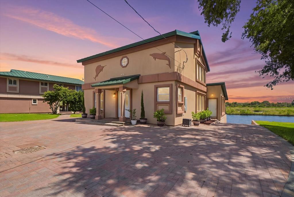A two-story tan house with green metal roofs sits beside a canal at sunset — 3194 INDIAN GULF LANE, HERNANDO BEACH, FL