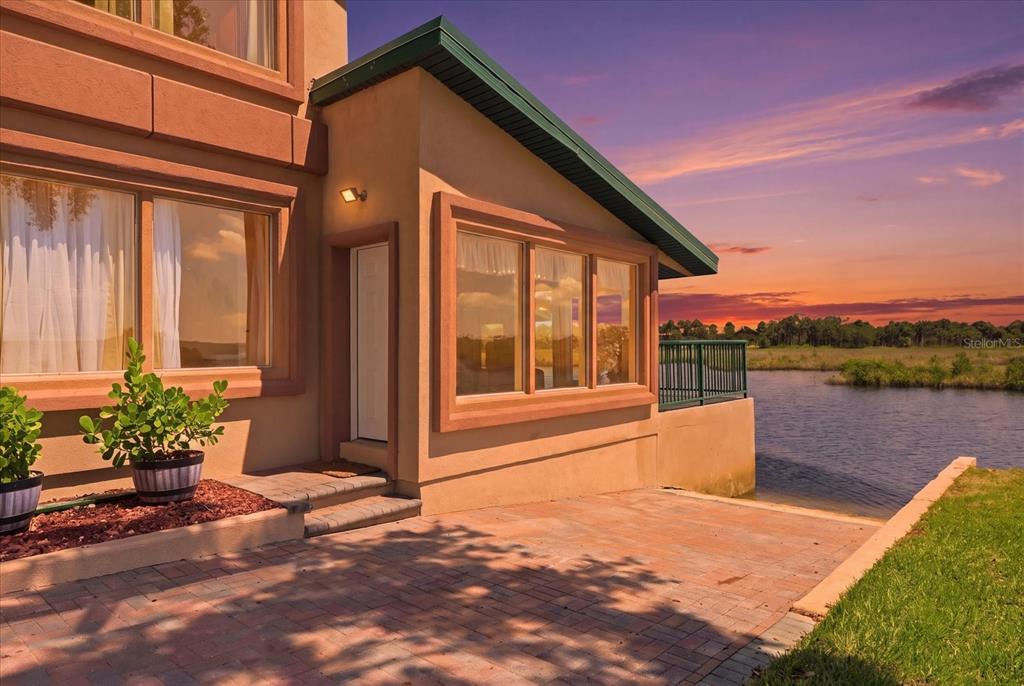 A tan house exterior with a paved patio, large windows, and a view of water — 3194 INDIAN GULF LANE, HERNANDO BEACH, FL