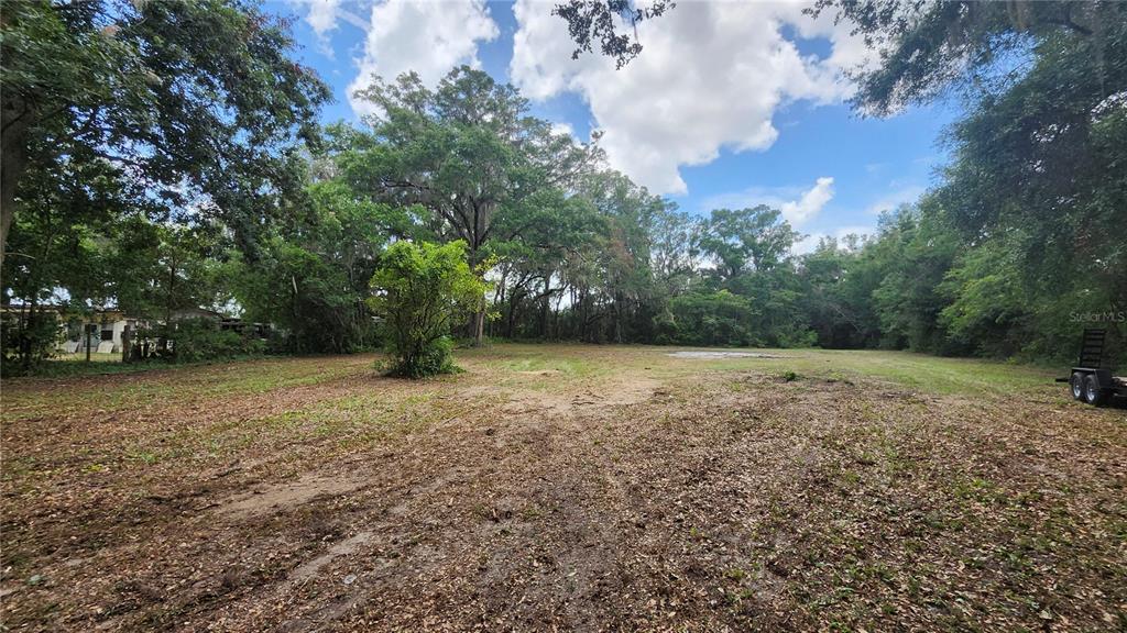 A cleared, grassy lot surrounded by mature trees under a partly cloudy sky — 7059 SE COUNTY HIGHWAY 25A, BELLEVIEW, FL