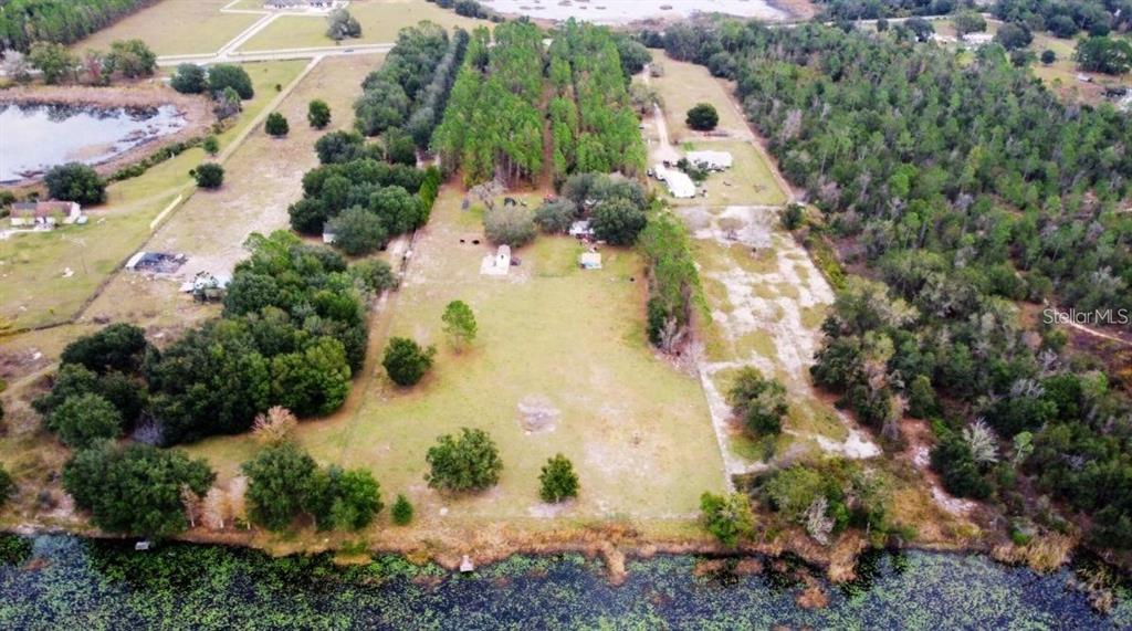 An aerial view shows a large grassy lot with trees, structures, and a waterfront edge — 19751 COUNTY ROAD 33, GROVELAND, FL