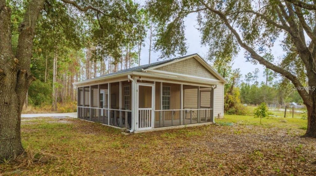 A small house with a large screened-in porch sits on a wooded lot — 19751 COUNTY ROAD 33, GROVELAND, FL