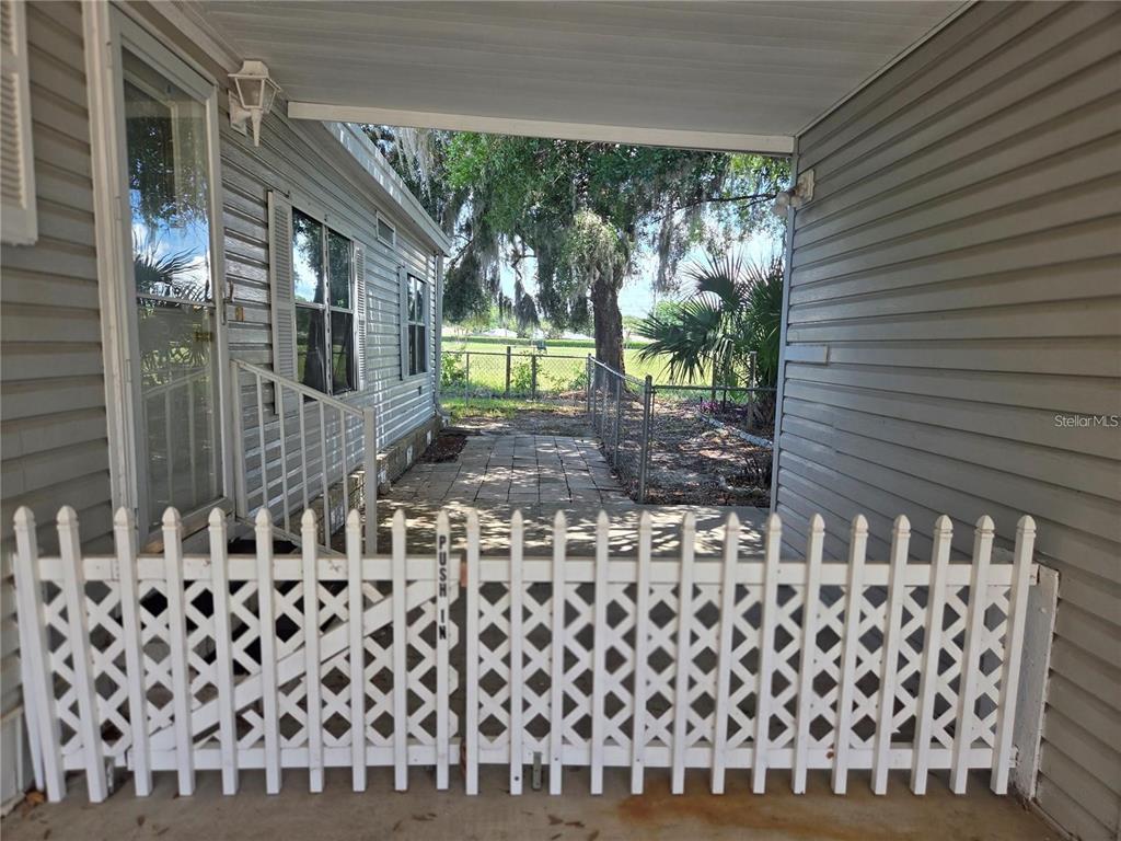 A white lattice gate stands on a concrete patio between two gray-sided exterior walls — 3224 MANATEE ROAD, TAVARES, FL