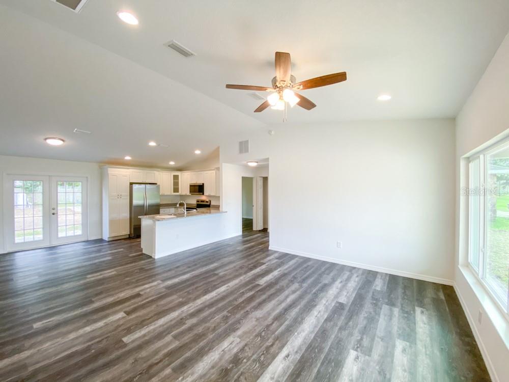A bright open-concept living area features wood-look flooring, a ceiling fan, and a white kitchen — 30 JUNIPER PASS LANE, OCALA, FL