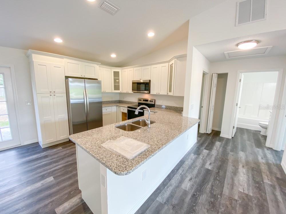 A kitchen with white cabinets, granite countertops, stainless steel appliances, and gray wood-look flooring — 30 JUNIPER PASS LANE, OCALA, FL