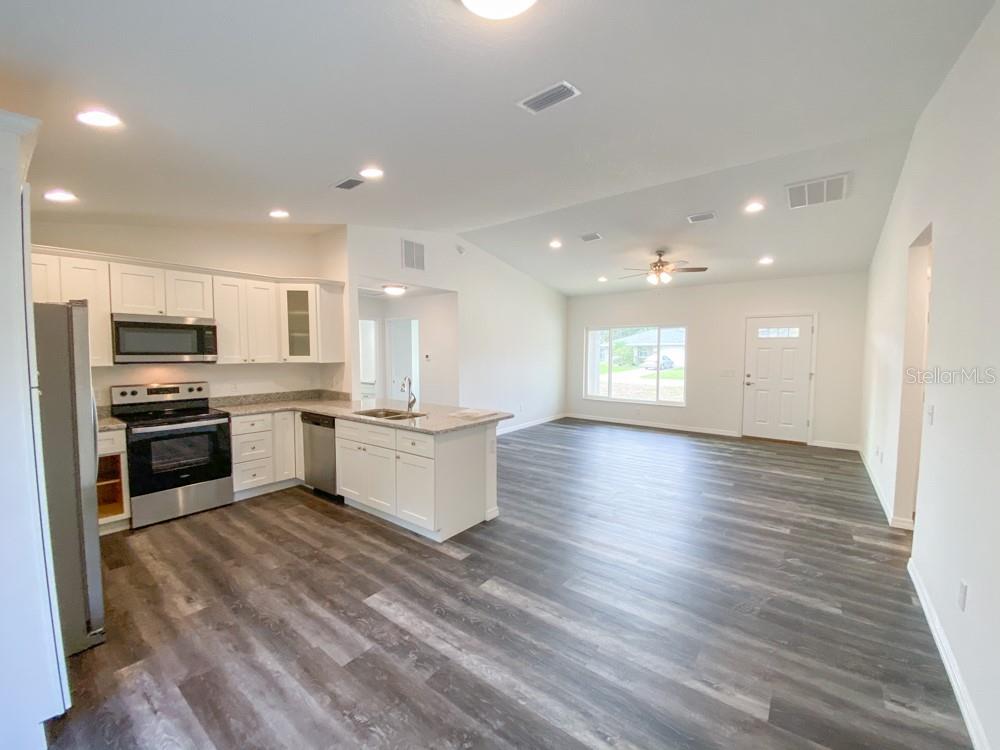 An open-concept kitchen and living area features white cabinets, stainless steel appliances, and wood-look flooring — 30 JUNIPER PASS LANE, OCALA, FL