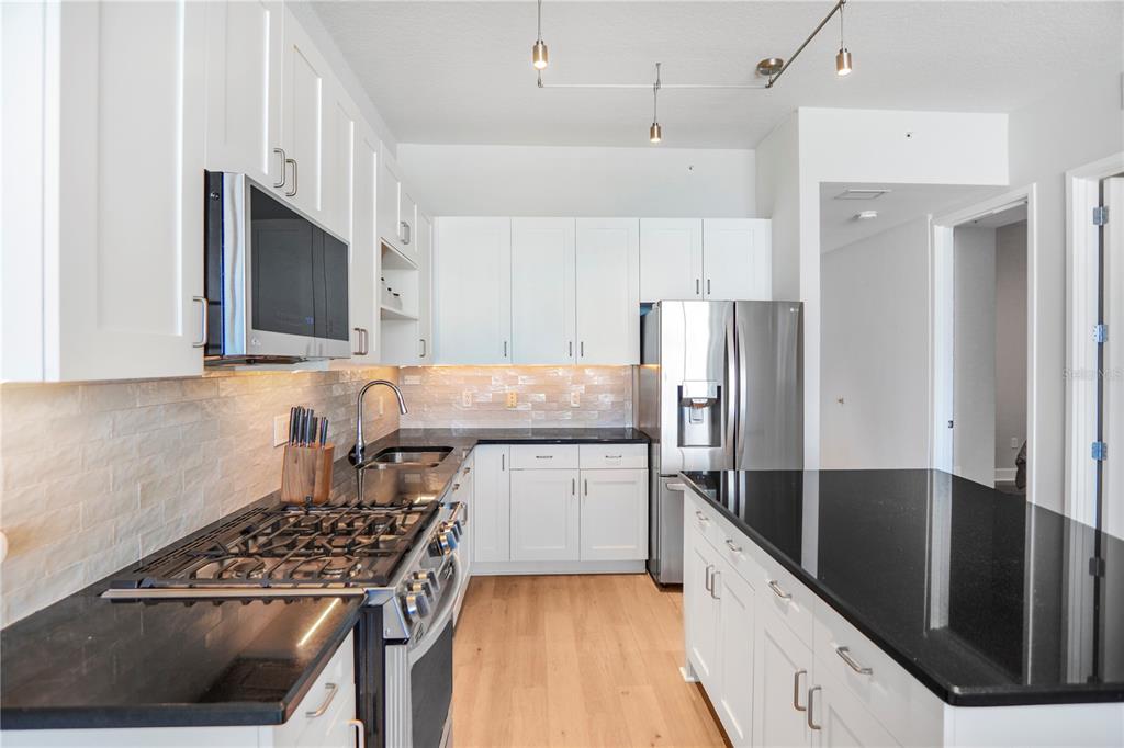 A modern kitchen features white cabinets, black countertops, stainless steel appliances, and light wood flooring — 150 E ROBINSON STREET UNIT 2608, ORLANDO, FL