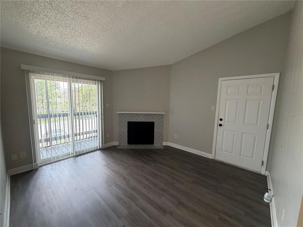 A living room features gray wood-look flooring, a fireplace, a sliding glass door, and white trim — 3716 IDLEBROOK CIRCLE UNIT 206, CASSELBERRY, FL