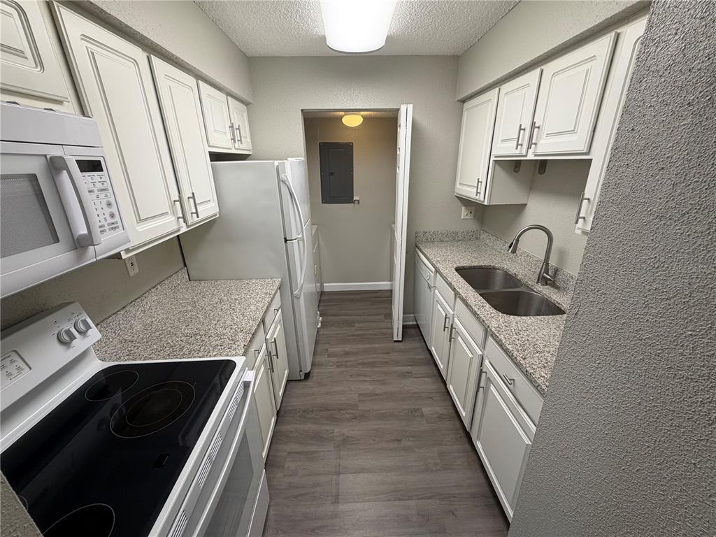 A galley kitchen features white cabinets, granite countertops, stainless steel appliances, and wood-look flooring — 3716 IDLEBROOK CIRCLE UNIT 206, CASSELBERRY, FL