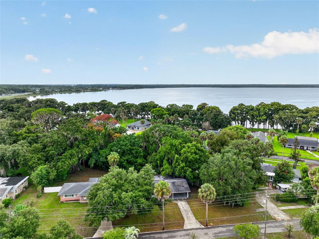 An aerial view shows a residential neighborhood with houses, lush trees, and a large lake — 1305 ORANGE AVENUE, TAVARES, FL