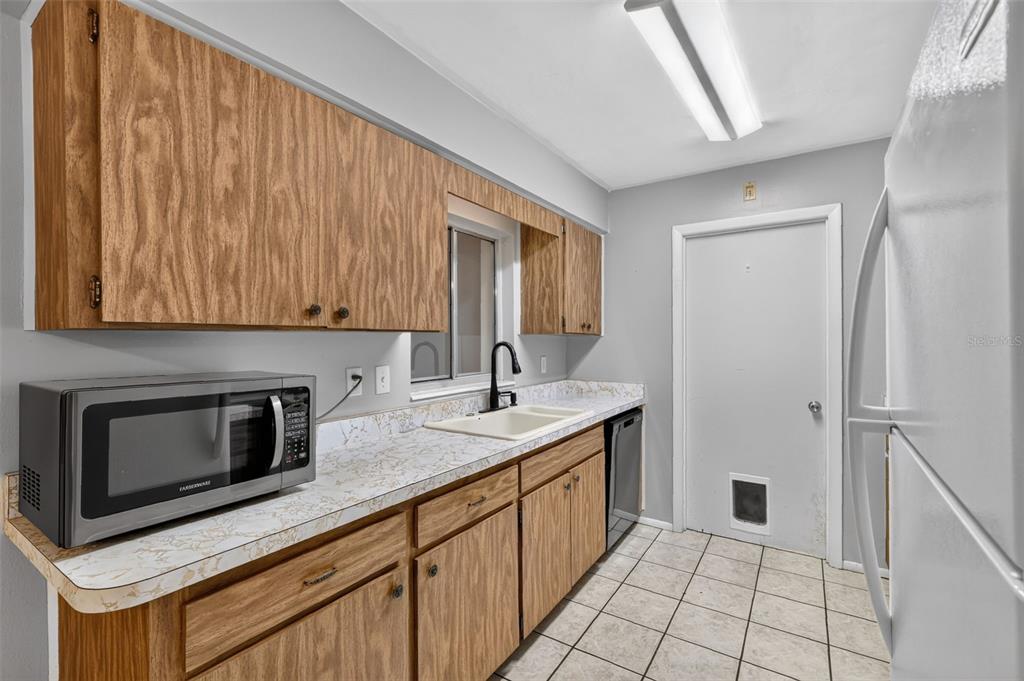 A kitchen features wood cabinets, a white countertop, a microwave, and a white tiled floor — 1305 ORANGE AVENUE, TAVARES, FL
