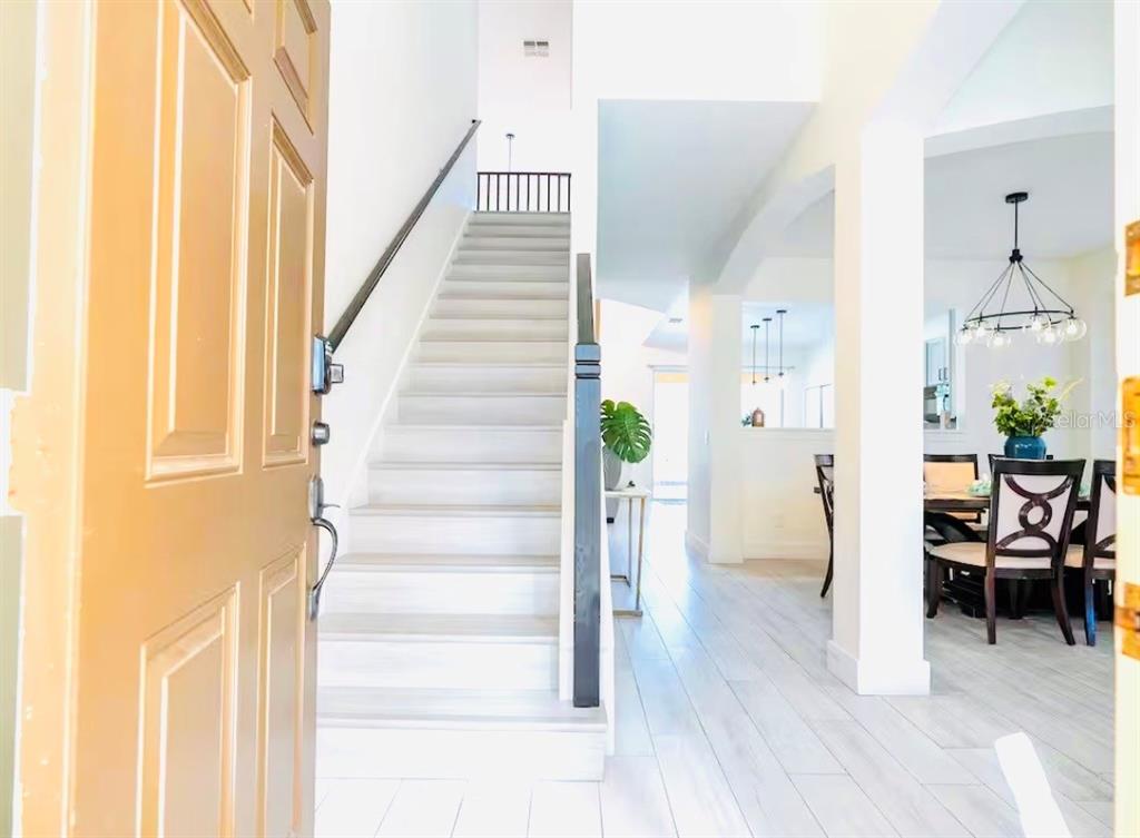 An entryway features a staircase with light wood flooring and a view into the dining area — 1078 ORANGE COSMOS BOULEVARD, DAVENPORT, FL