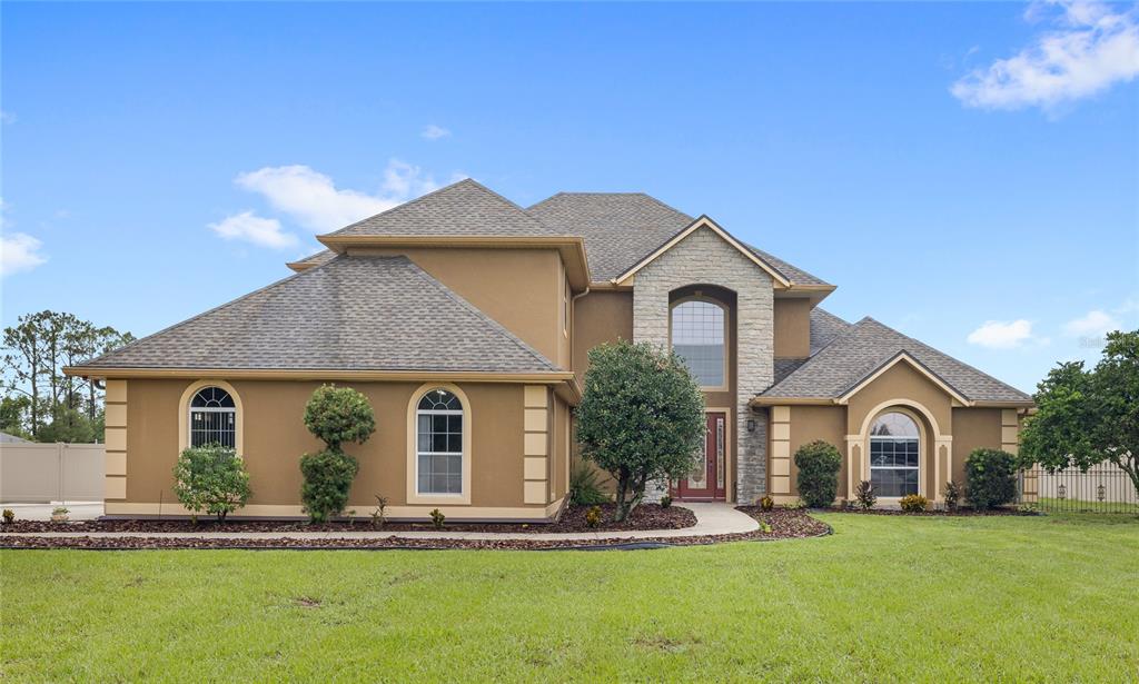 A two-story house with a tan stucco exterior, stone facade, and a multi-gabled shingled roof — 12901 PHILLIPS ROAD, GROVELAND, FL