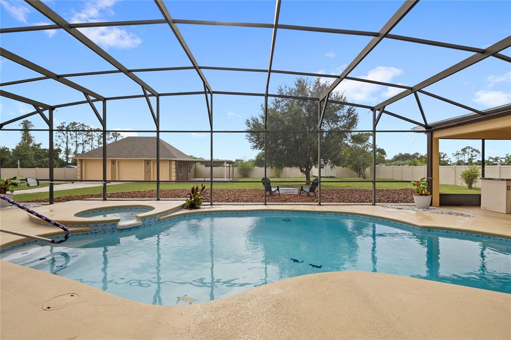 A screened-in pool and hot tub area with a view of a backyard and garage — 12901 PHILLIPS ROAD, GROVELAND, FL