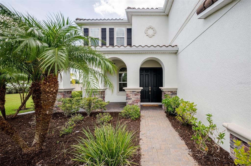 A paved walkway leads to the arched entryway of a white house with stone accents — 4789 VASCA DRIVE, SARASOTA, FL
