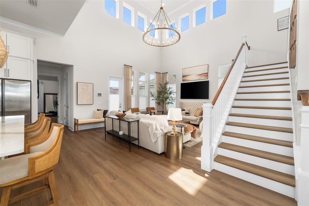 A bright, open-concept living room features a high ceiling, a chandelier, and a wooden staircase — 2509 SW 120TH DRIVE, GAINESVILLE, FL