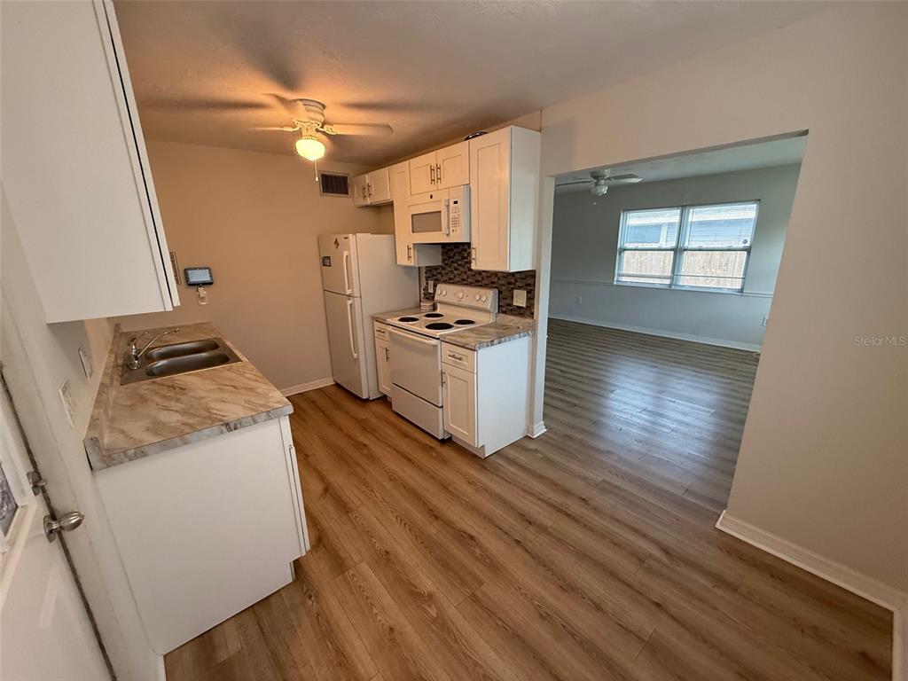 A kitchen with white cabinets, white appliances, and wood-look flooring opens into a living area — 2217 20TH AVENUE W, BRADENTON, FL