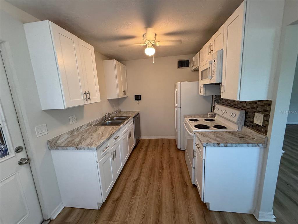 A kitchen features white cabinets, marble-patterned countertops, a white stove, and wood-look flooring — 2217 20TH AVENUE W, BRADENTON, FL