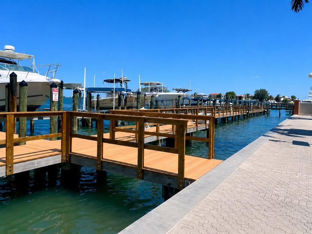 A wooden pier extends over the water toward several docked boats under a clear sky — 5353 GULF BOULEVARD UNIT A401, ST PETE BEACH, FL
