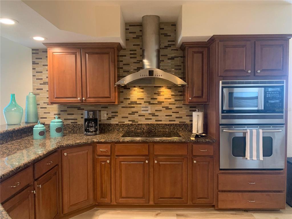 A kitchen with wood cabinets, granite countertops, a stainless steel range hood, and tile backsplash — 5353 GULF BOULEVARD UNIT A401, ST PETE BEACH, FL