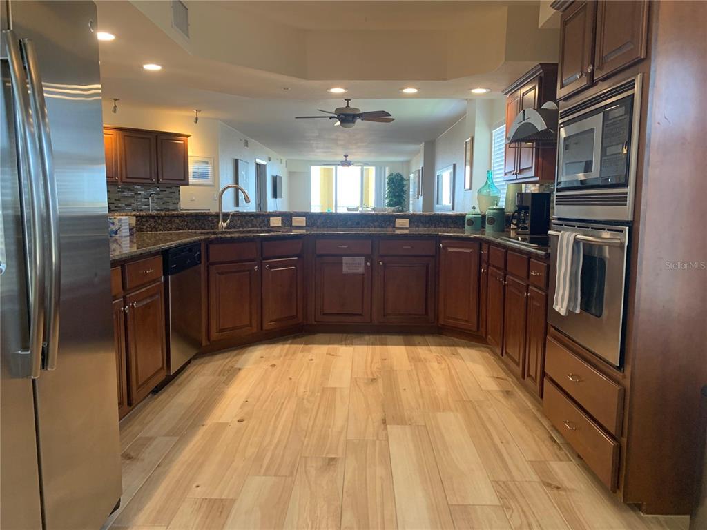 A kitchen with wood cabinets, granite countertops, stainless steel appliances, and light wood-look flooring — 5353 GULF BOULEVARD UNIT A401, ST PETE BEACH, FL
