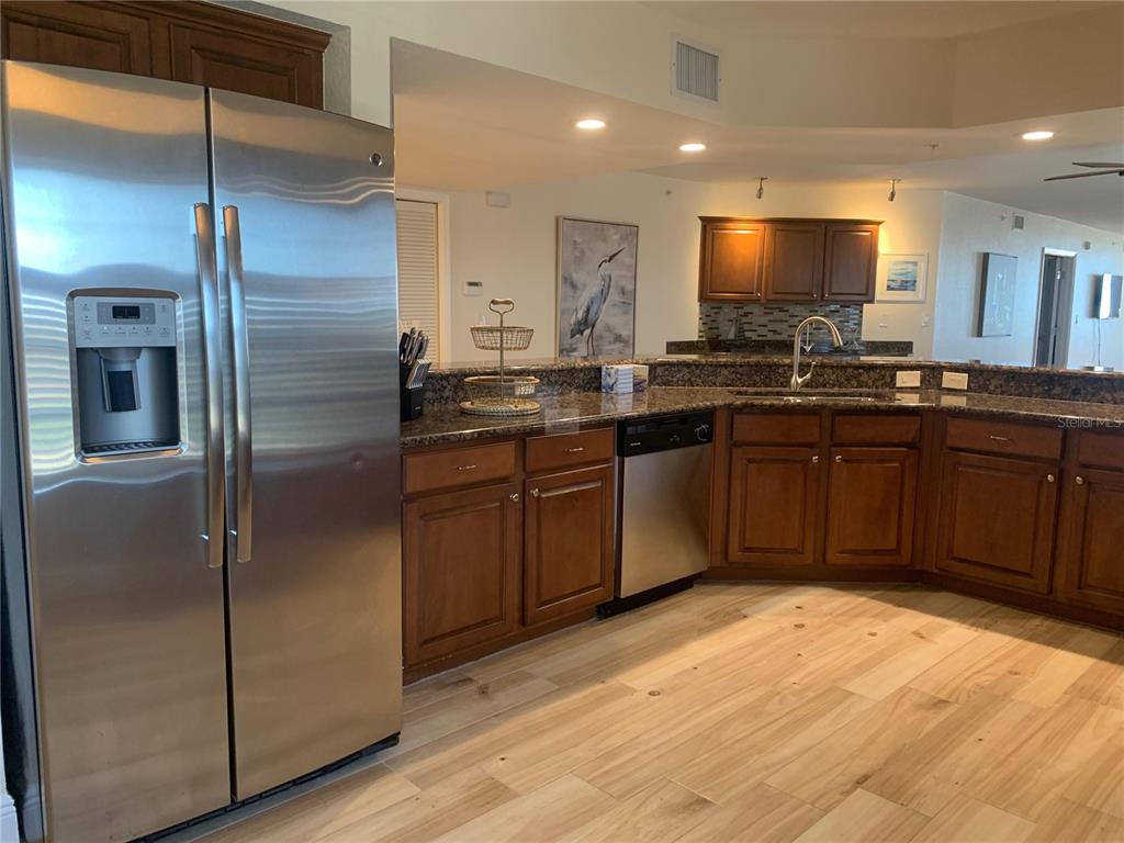 A kitchen features stainless steel appliances, wood cabinets, granite countertops, and light wood-look flooring — 5353 GULF BOULEVARD UNIT A401, ST PETE BEACH, FL